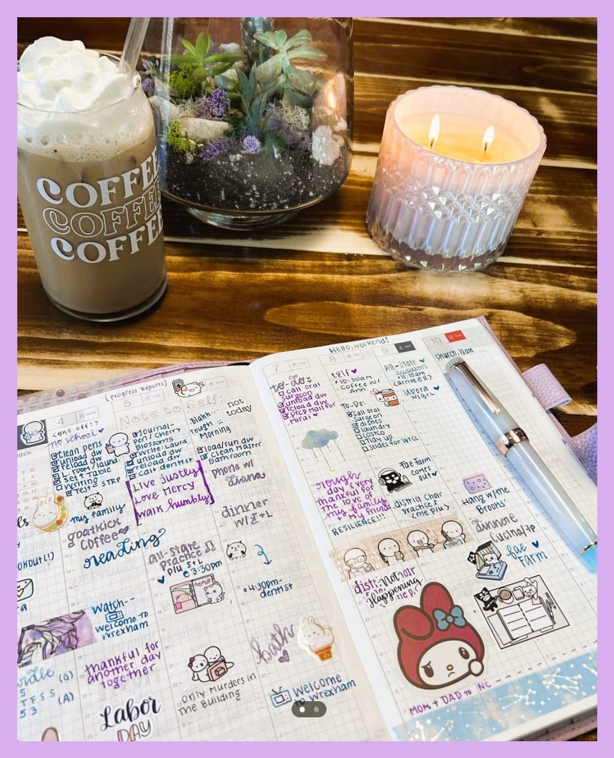 Photo of an open planner on a wooden desk with a fountain pen on top. Behind there is a tall glass of iced coffee, a terrarium, and a 2-wick candle. 